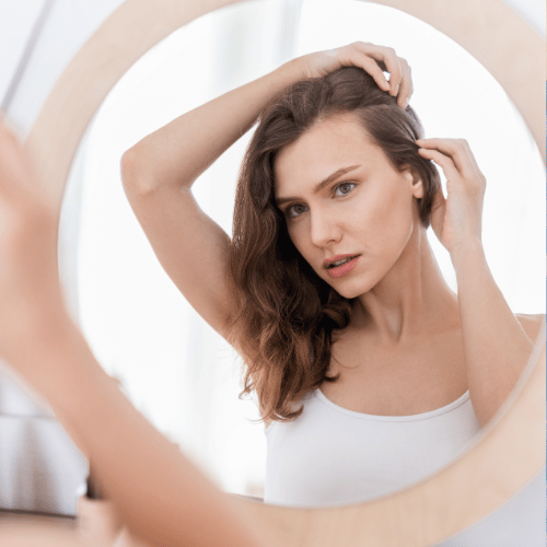 Young woman checking for thinning hair in mirror at home
