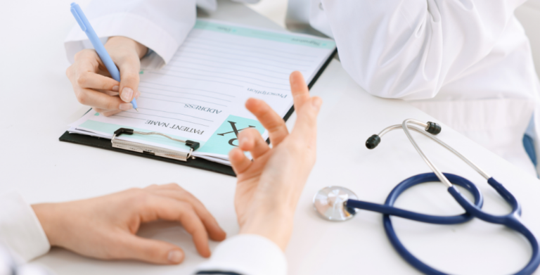 A doctor records notes on a clipboard as a patient watches, indicating a consultation in a medical office.